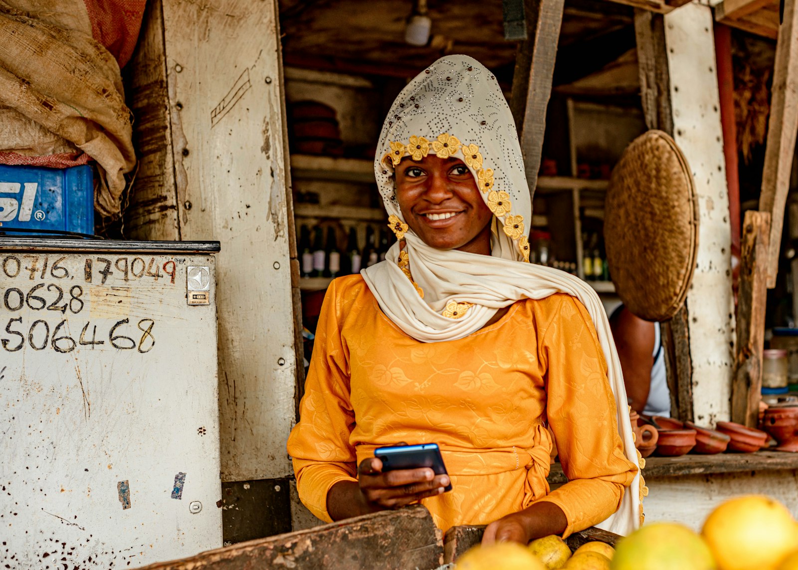 A woman at a fruit stall smiling at her phone