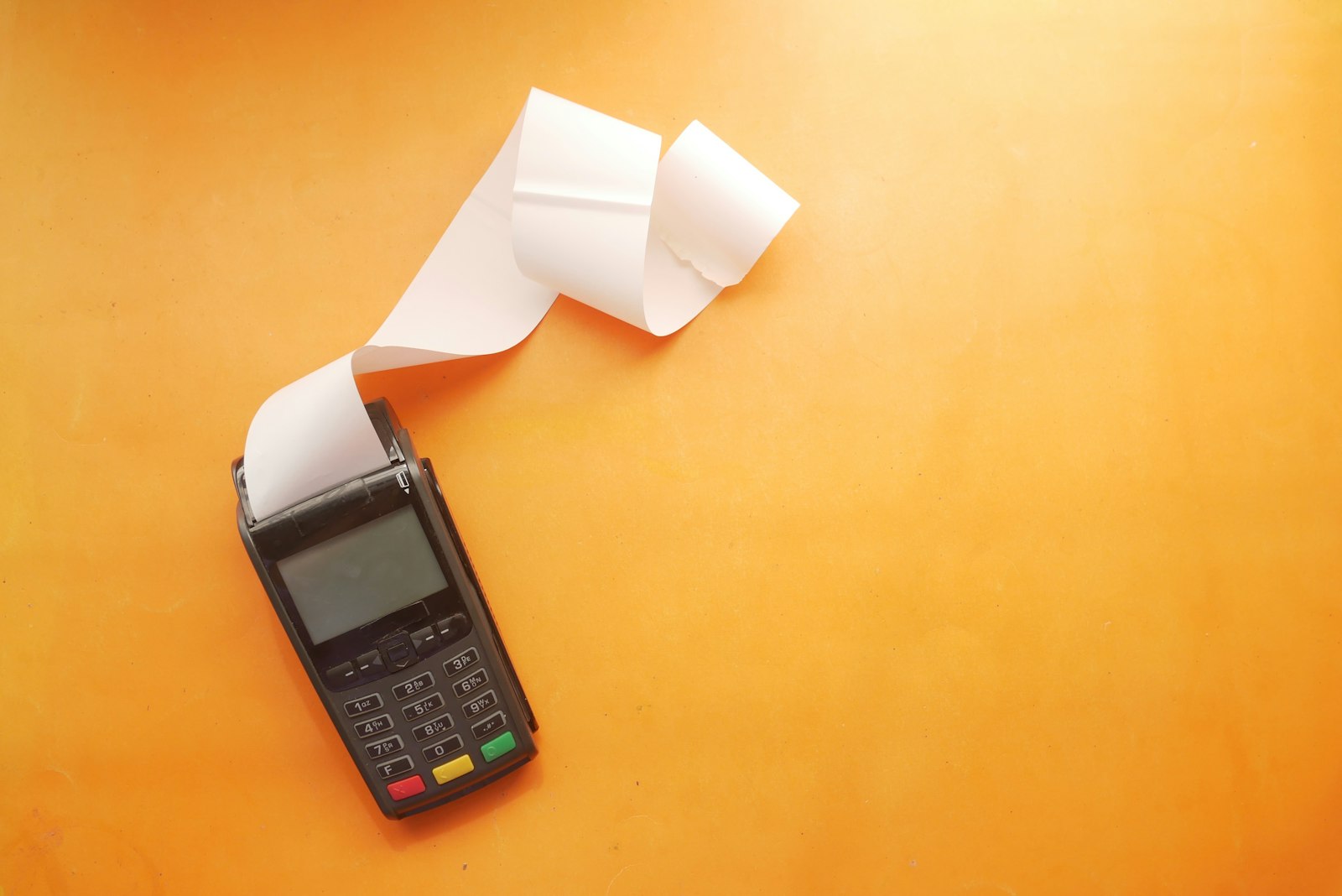 A card machine printing a receipt on an orange background