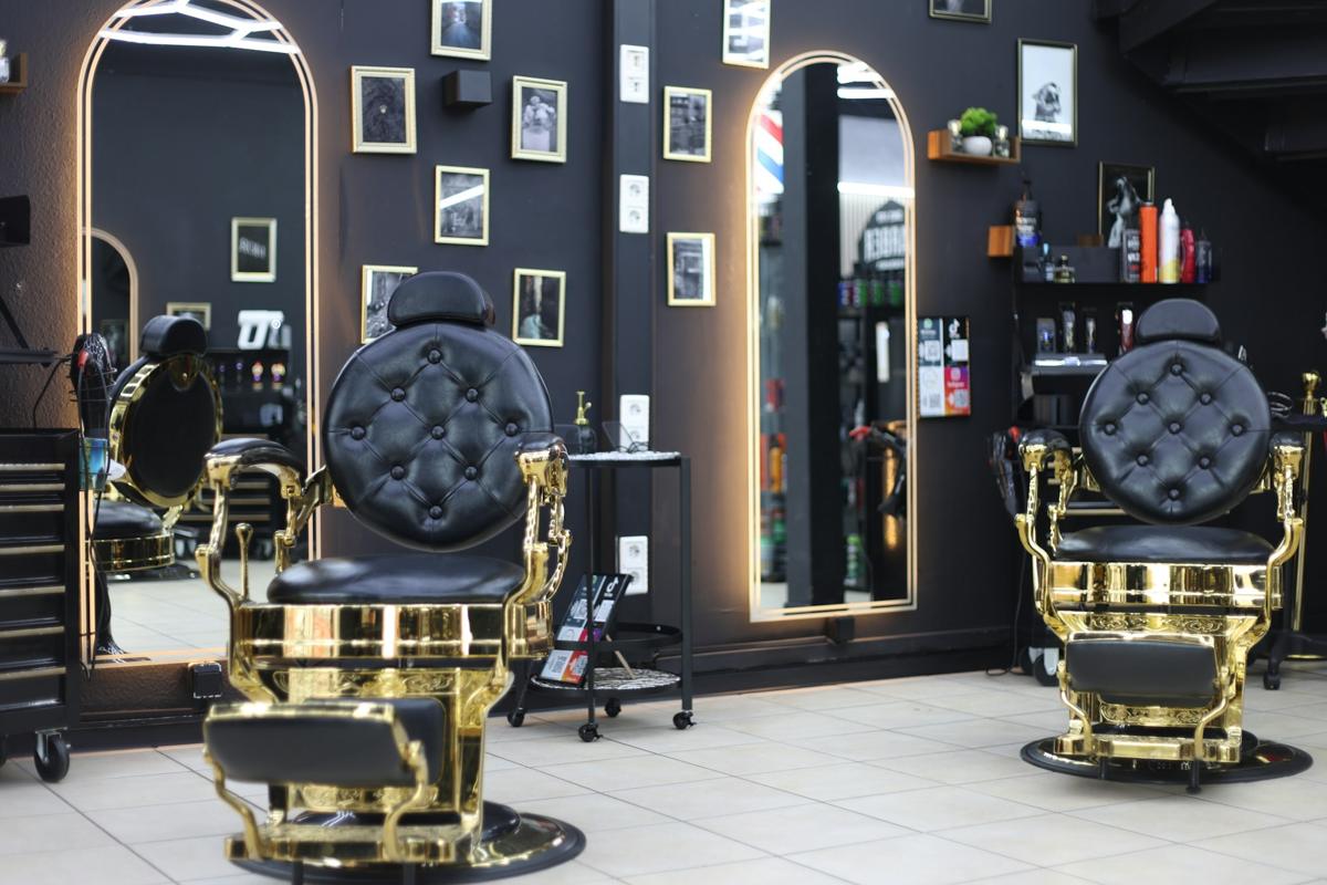 Two black and gold barber chairs in a dark salon